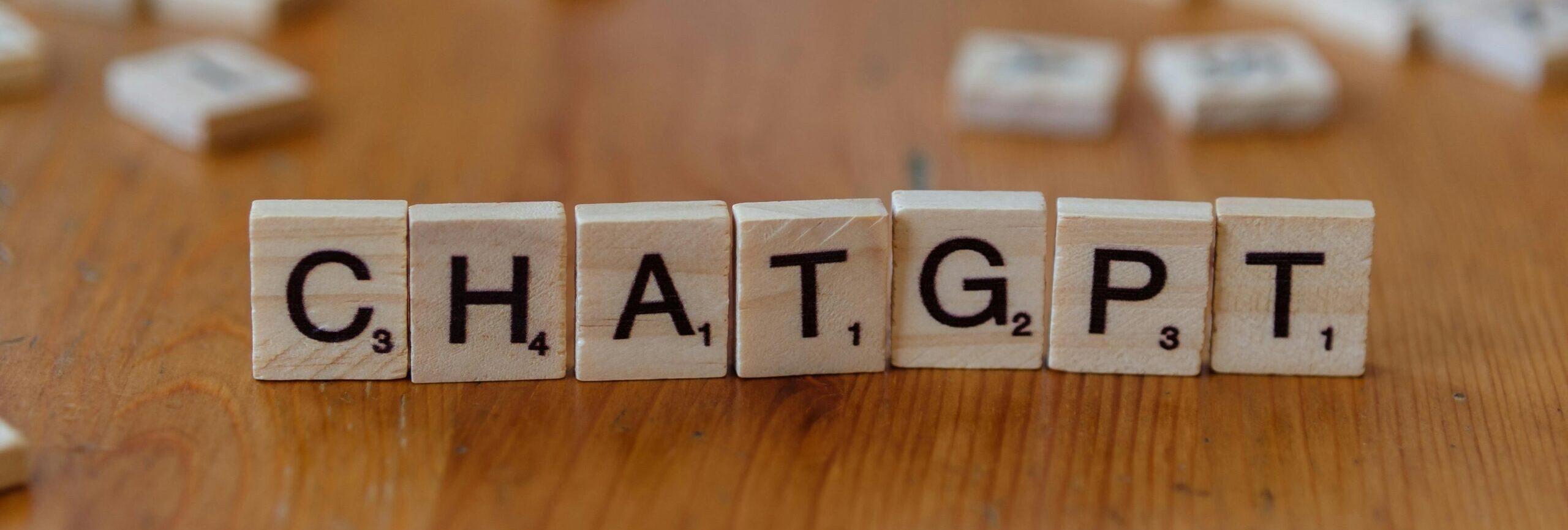 Scrabble tiles spelling "CHATGPT" on wooden surface, emphasizing AI language models.
